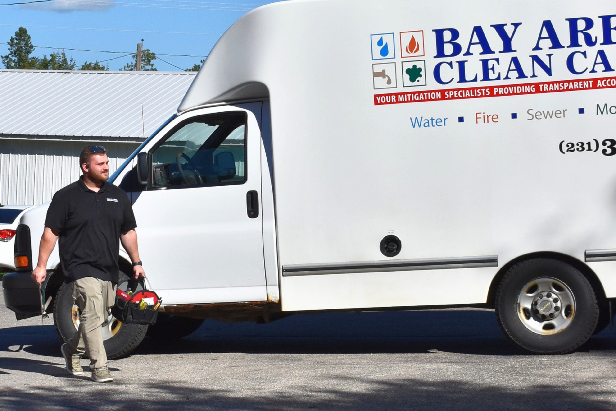 A Bay Area Clean Care technician carrying a tool bag past the restoration truck
