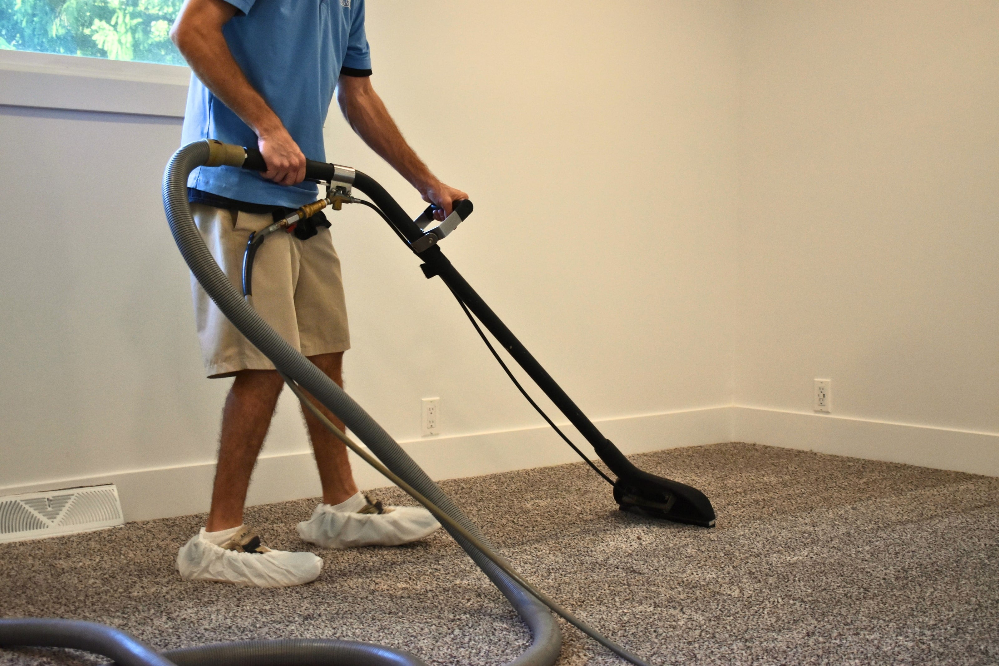 A technician in shoe covers cleaning carpet with a hot water extraction wand