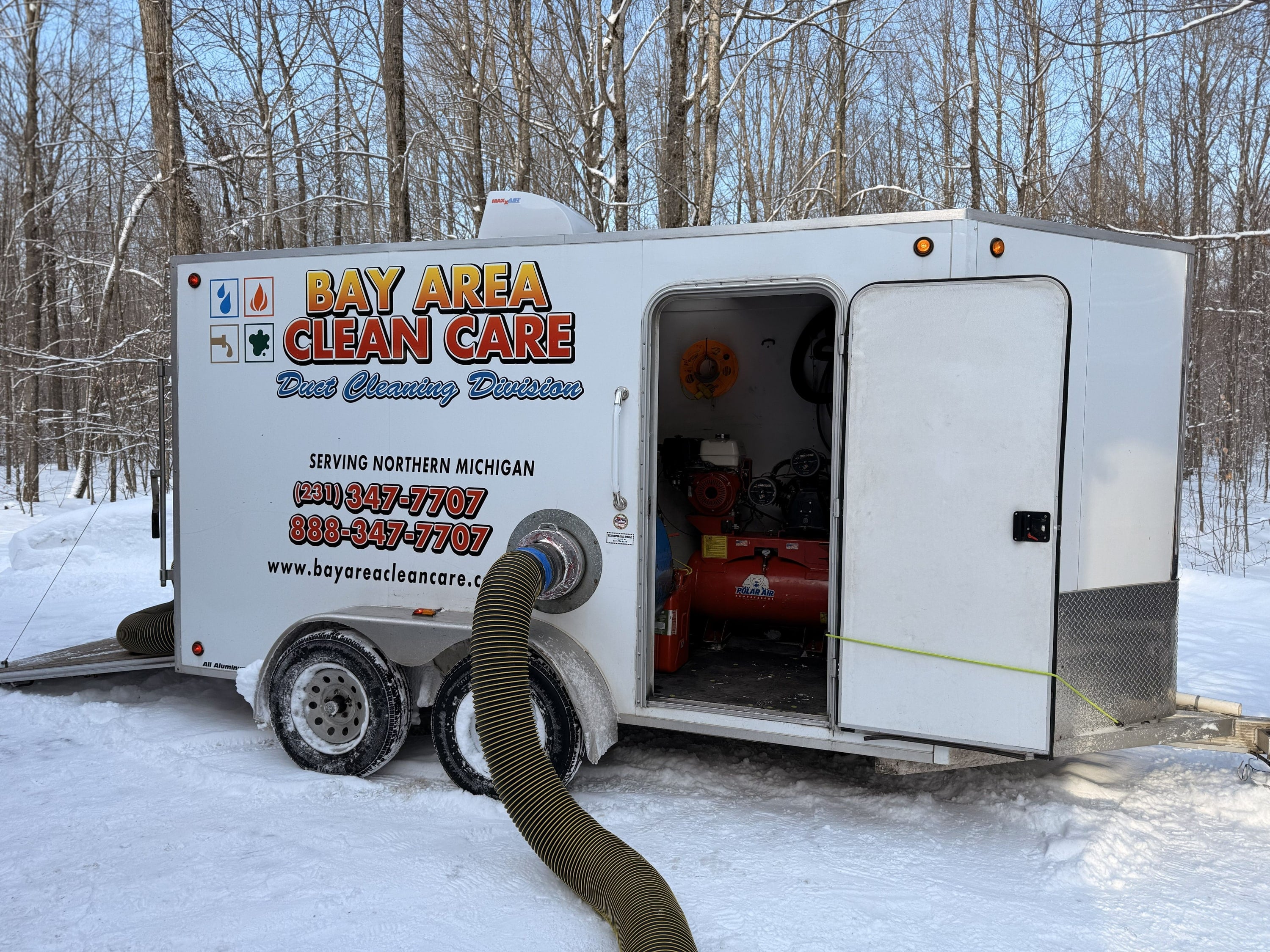 The Bay Area Clean Care duct cleaning trailer with its vacuum hose out, parked in the snow
