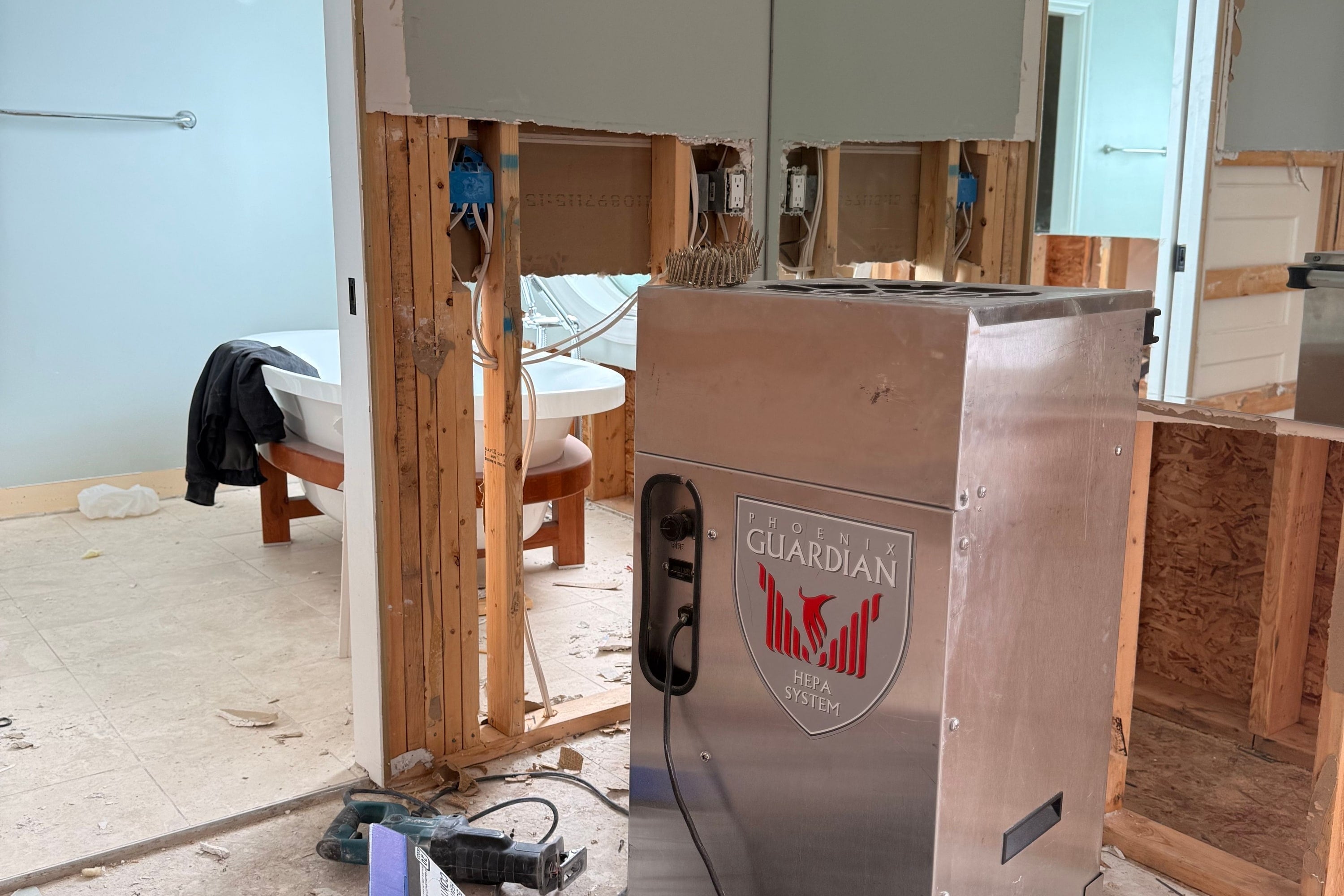 A stainless steel HEPA air scrubber running in a bathroom opened up to the studs