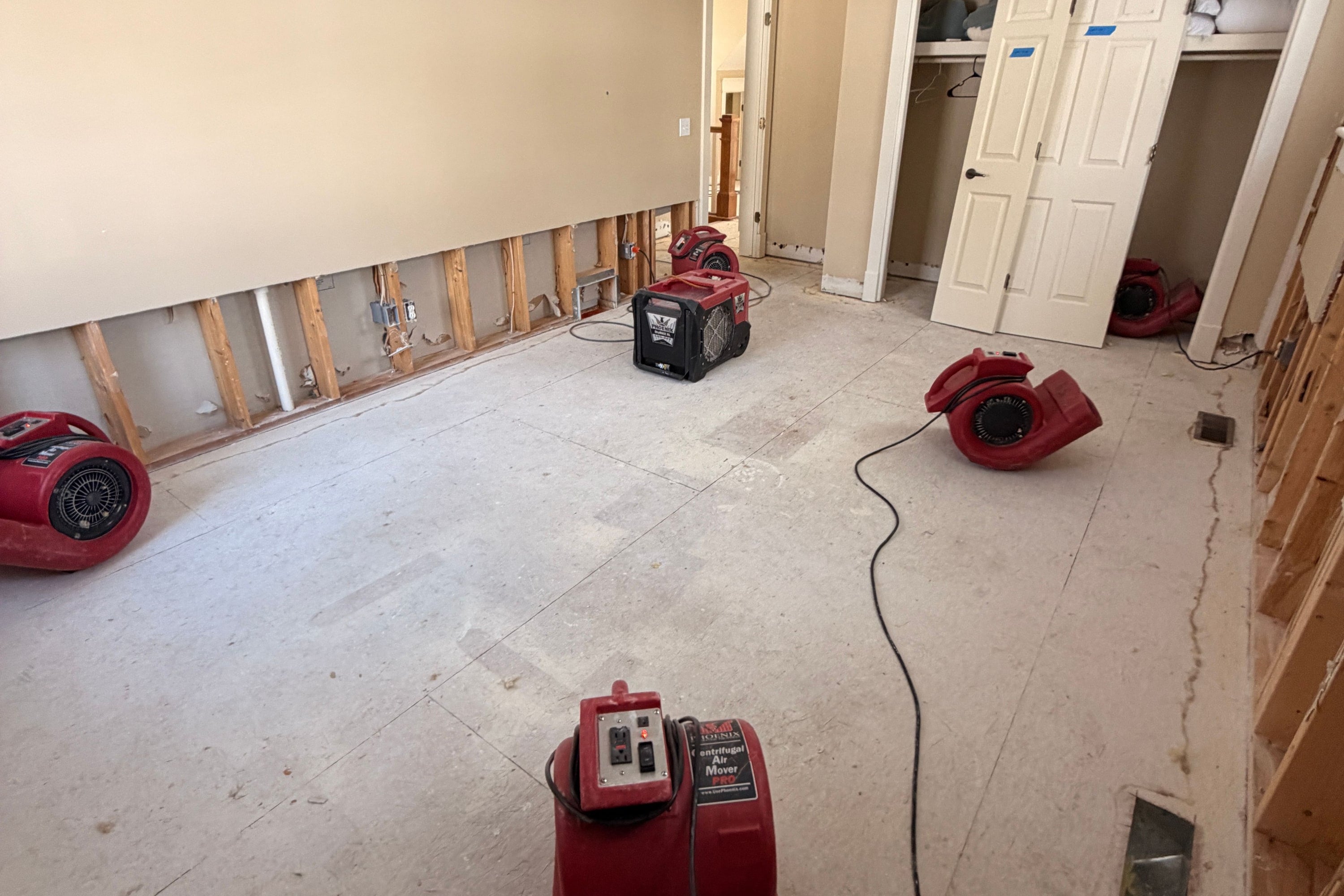 Red air movers and a dehumidifier drying a room after the wet drywall was cut away